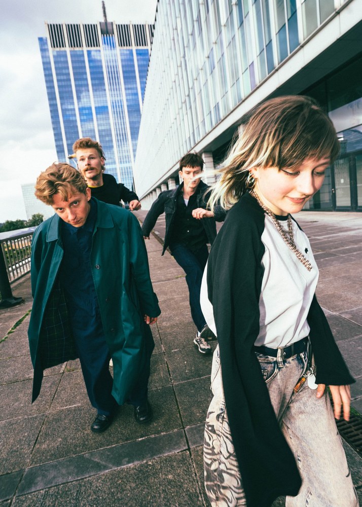 De bandleden van Eosine lopen voorbij een groot gebouw